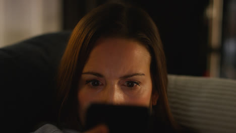 Close-Up-Of-Anxious-Woman-Sitting-On-Sofa-At-Home-At-Night-Looking-At-Mobile-Phone-Concerned-About-Social-Media-Or-Bad-News-1